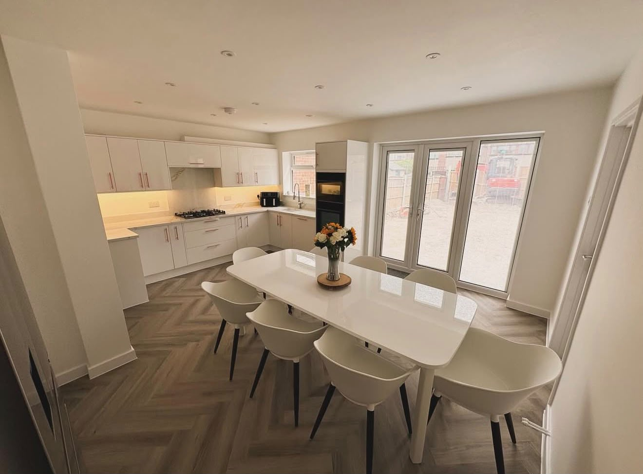 Full refurbishment kitchen-diner with white gloss cabinetry, herringbone flooring and French doors to garden